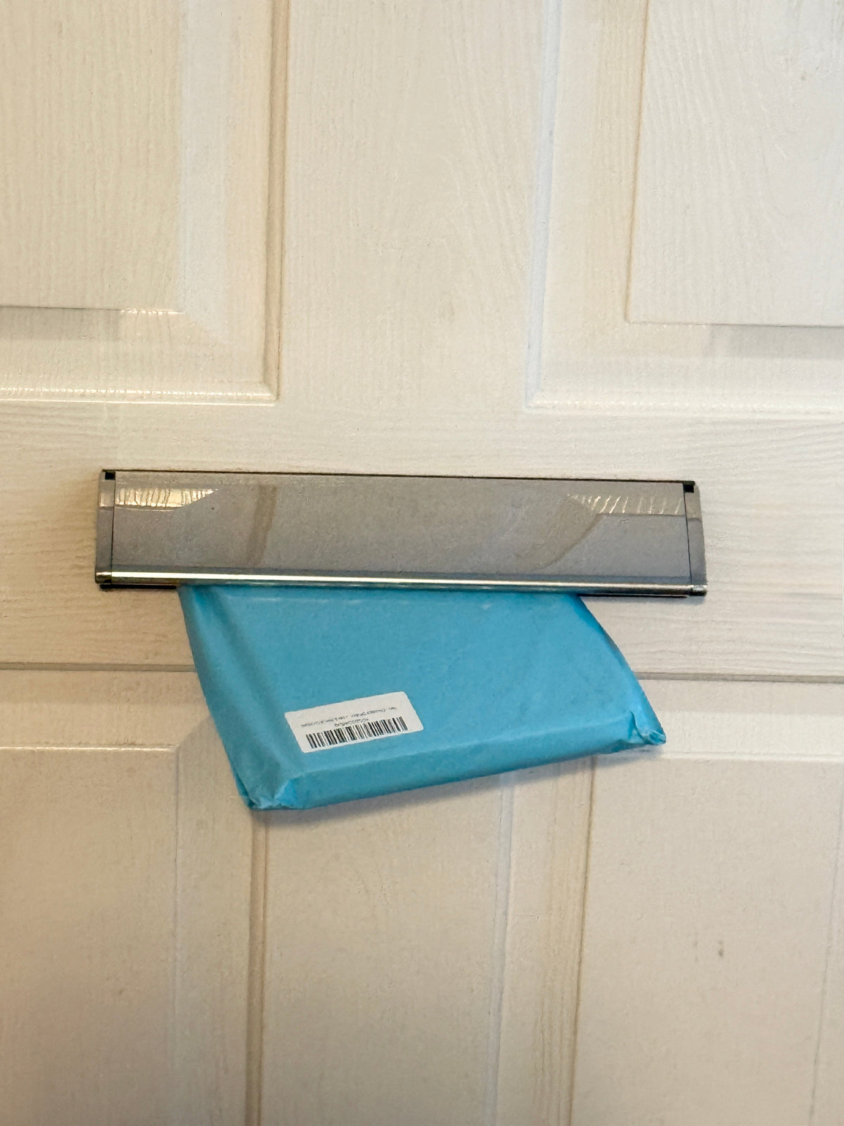 Slim light blue letterbox gift box being posted through a front door